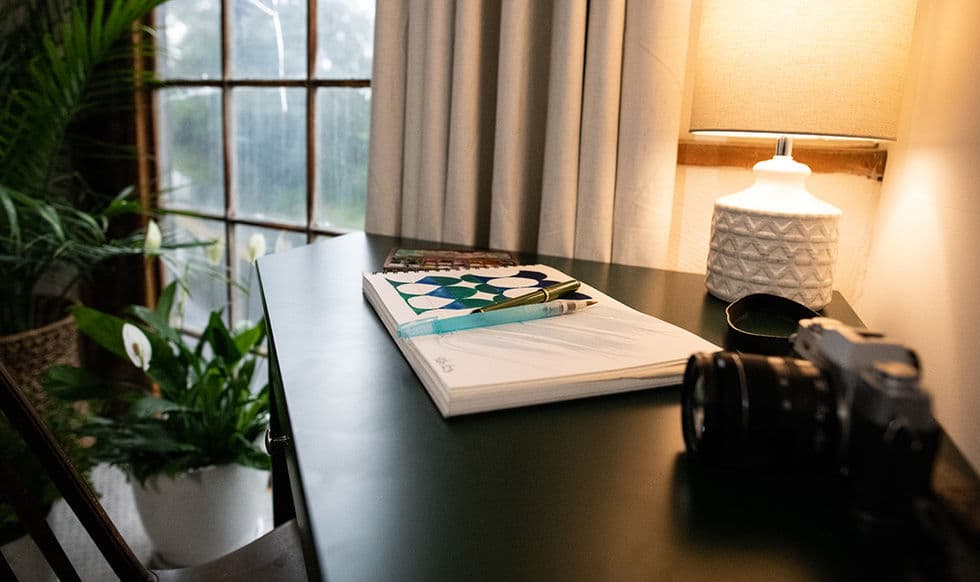 Writing desk with chair and table lamp next to a multi-paned window.