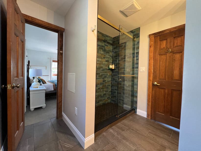 A bathroom featuring a beautifully tiled walk-in shower. An open doorway leads to the bedroom.