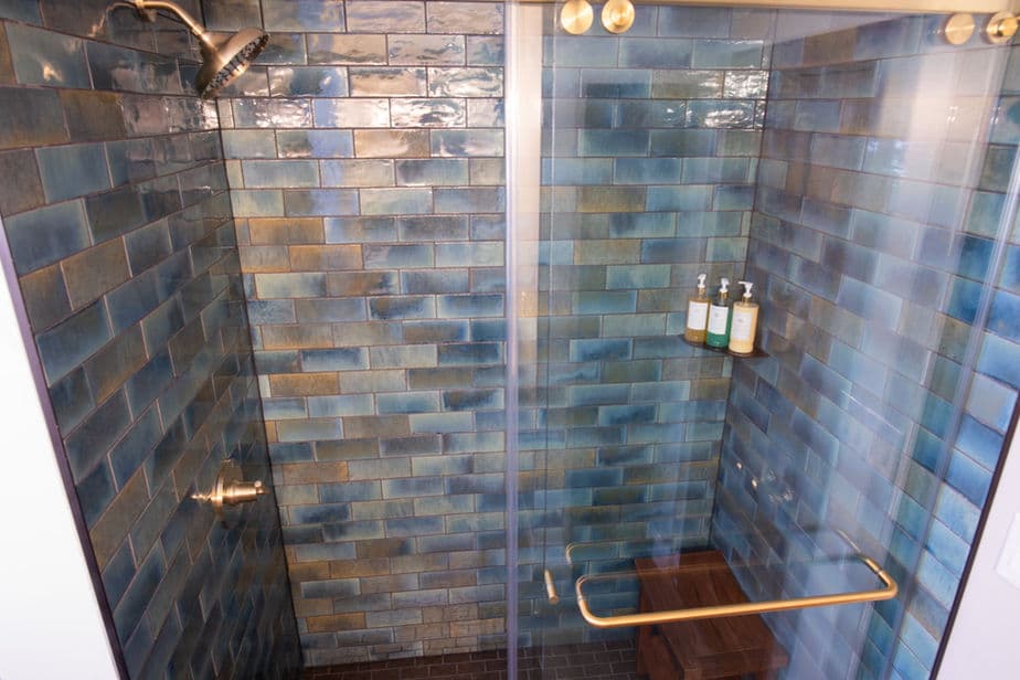 Walk-in shower that's tiled in blues, greens and neutrals, with gold-toned fixtures.