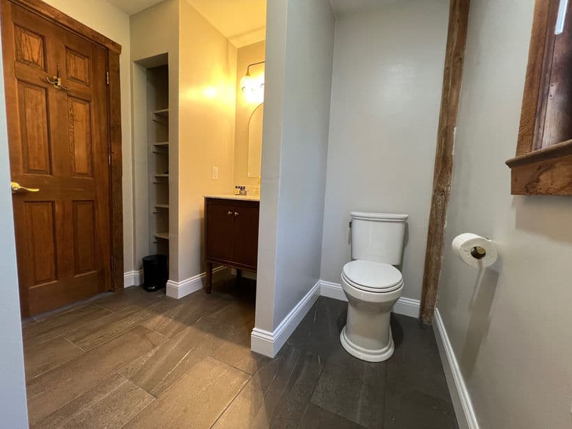 Bathroom with built-in shower, vanity sink, and toilet. There is a privacy wall between the sink and toilet area.