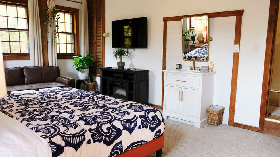 Light-filled bedroom with king bed, loveseat, dresser, and wall-mounted smart TV.