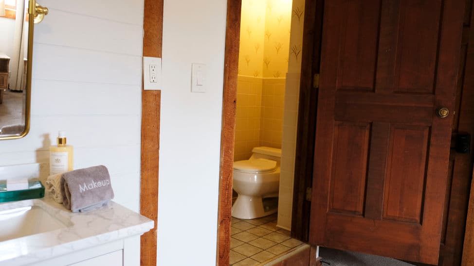 An open door leads from the bedroom to the bathroom with shower and toilet. The sink is located in the bedroom.