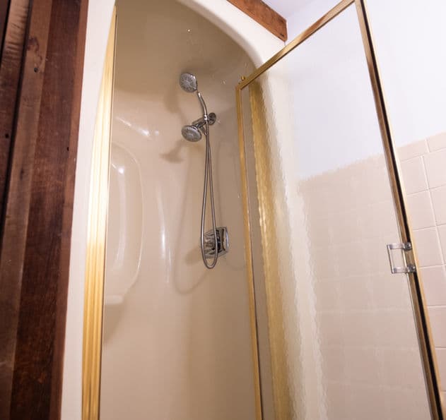 Stand-up shower with glass door and handheld shower head.