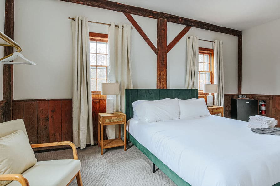 Bedroom with king-size bed, two armchairs, and lots of natural light coming from several windows.