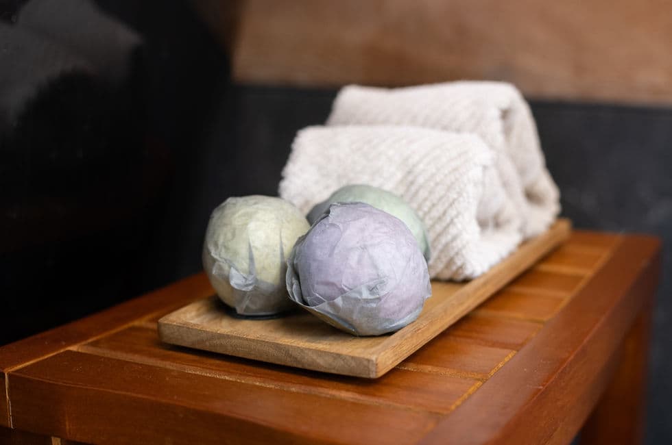 A wooden bench with wrapped bath soaps and plush rolled towels on top.