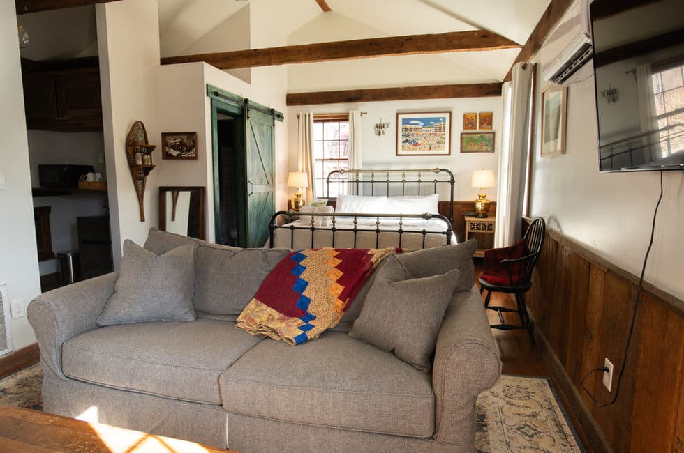 A comfy sitting area with a deep loveseat, a lap blanket, and a wall-mounted flat-screen TV. The bed is visible in the background.