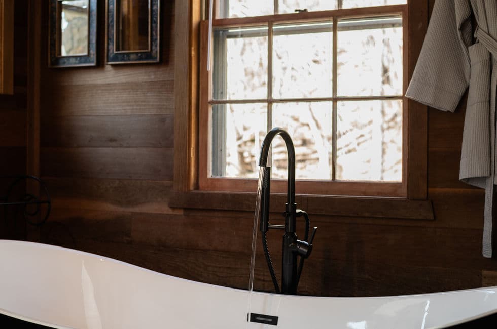 A window lets sunlight stream in on the goose neck faucet and gleaming white interior of the vintage style slipper tub.