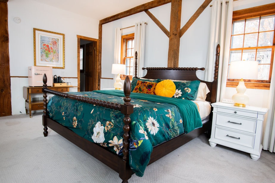 A spacious bedroom with lots of natural light, a king four-poster bed, and matching nightstands with table lamps.
