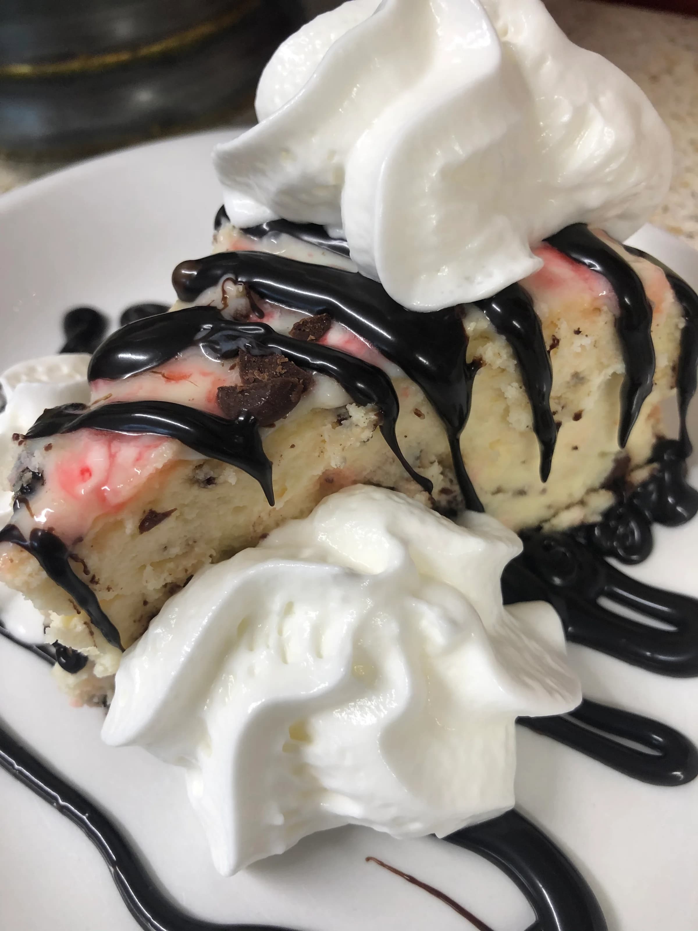 A slice of ice cream cake topped with whipped cream and chocolate syrup.