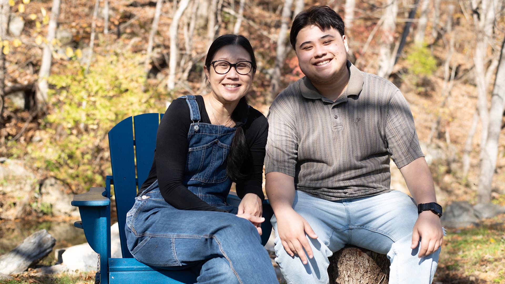 A woman and a young man smile while sitting outdoors on a sunny day.