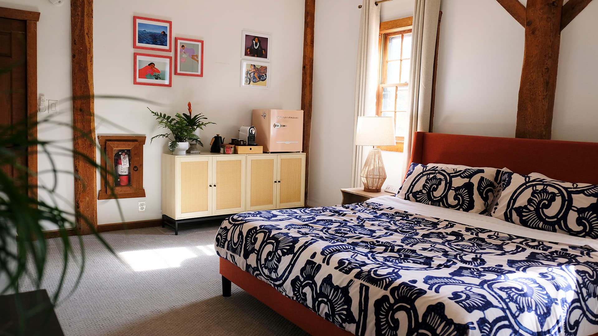 A cozy bedroom featuring a patterned bedspread, wooden beams, a vintage-style fridge, and colorful wall art.