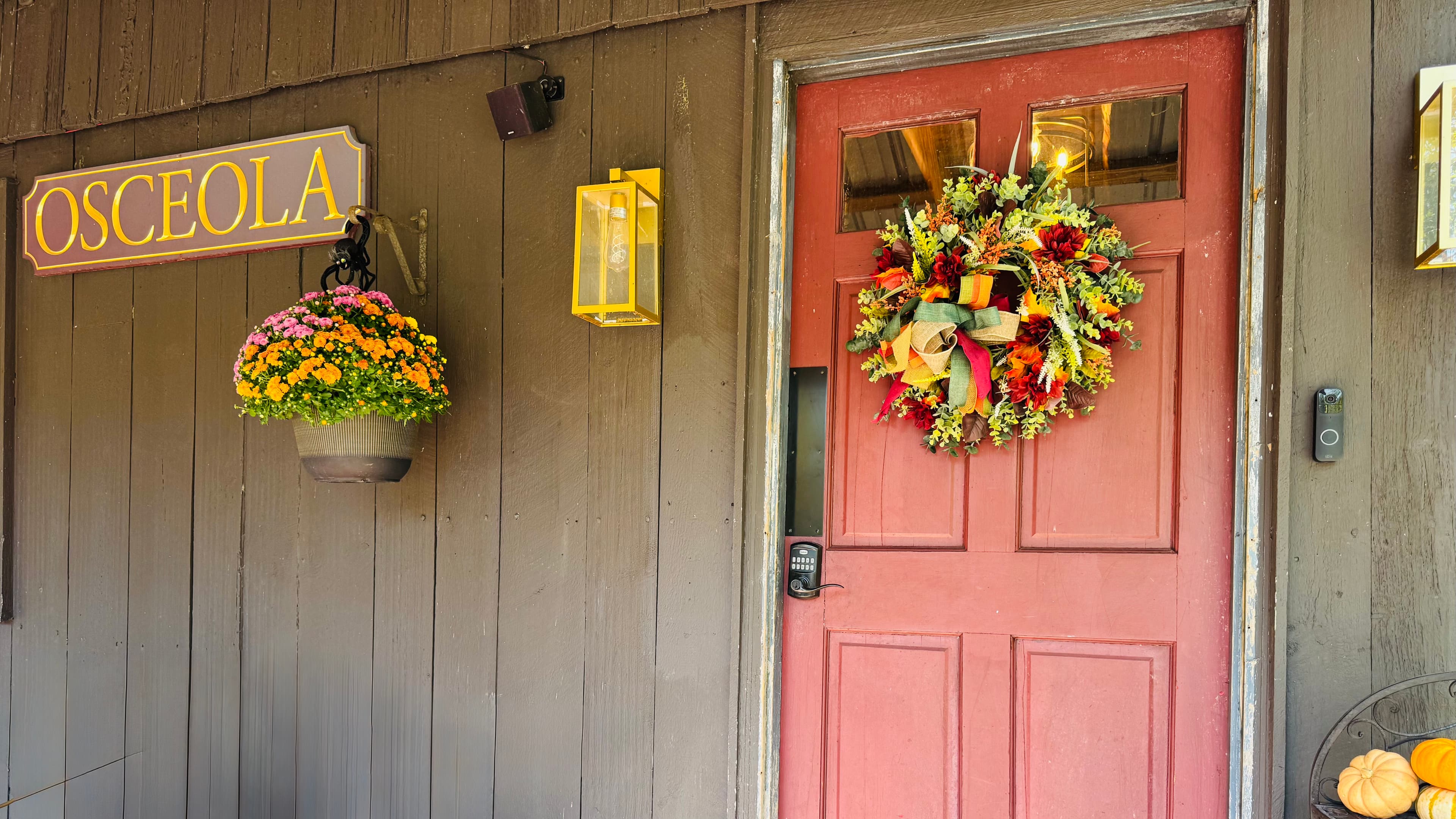 A red door adorned with a colorful wreath, against a wooden wall featuring a sign that says "Osceola."