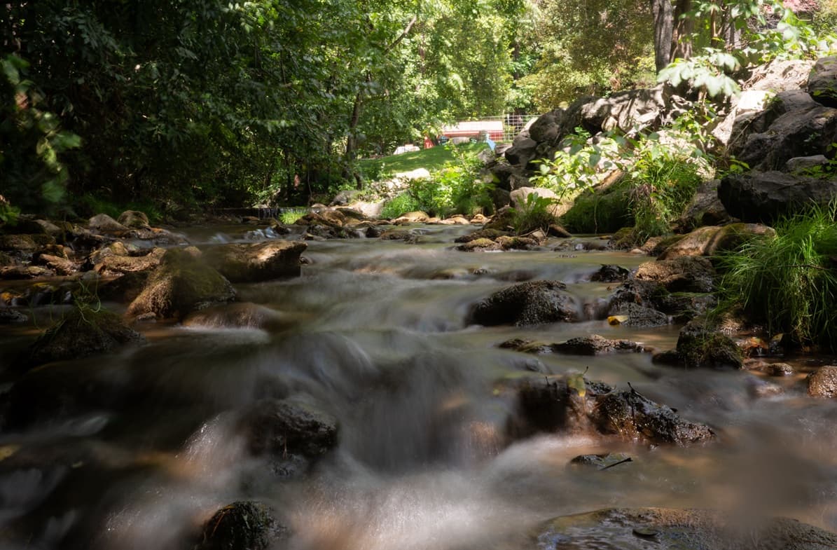 A serene stream flows over rocks, surrounded by lush greenery.