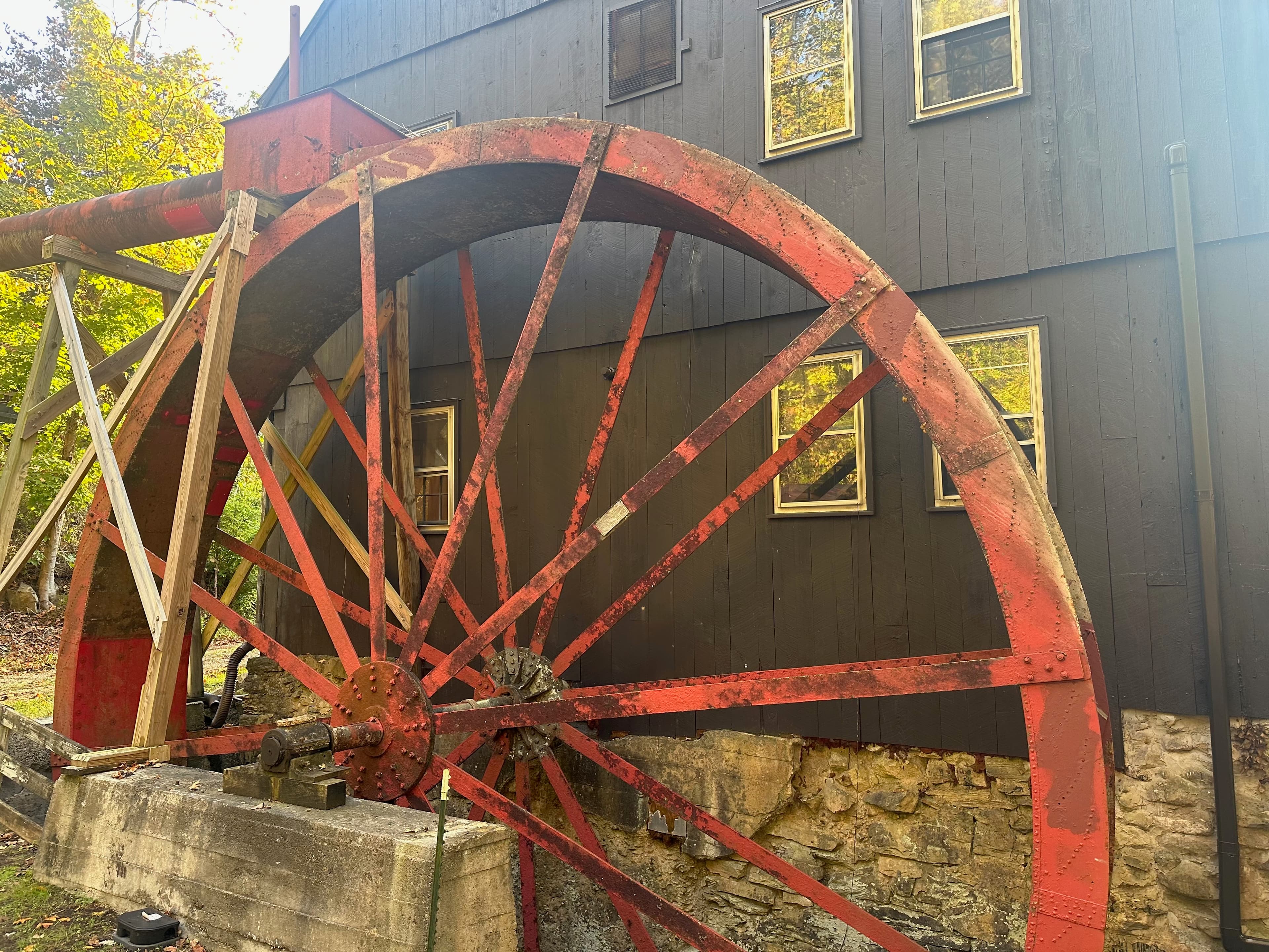 A large, weathered red waterwheel stands beside a black wooden building with multiple windows.