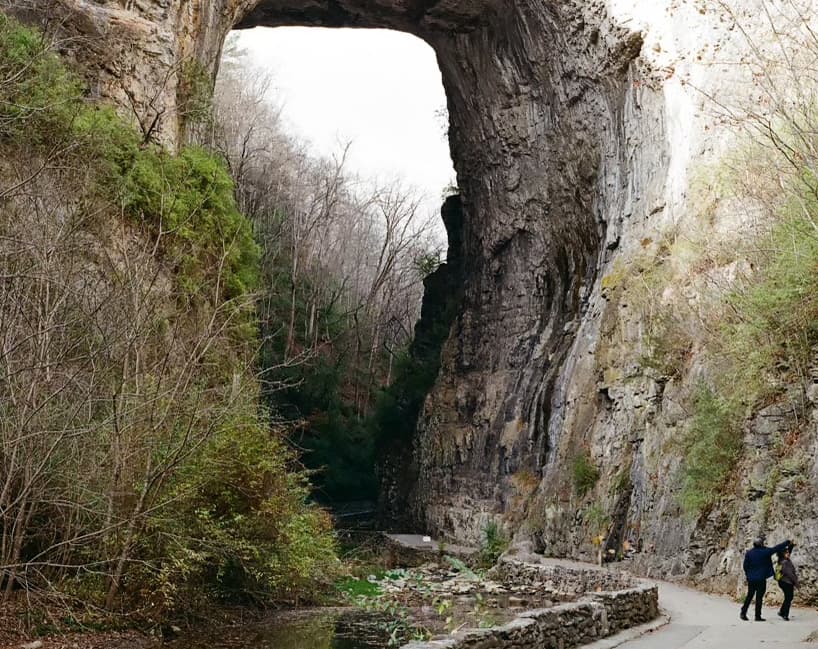 A large stone archway towers over a pathway where two people walk.