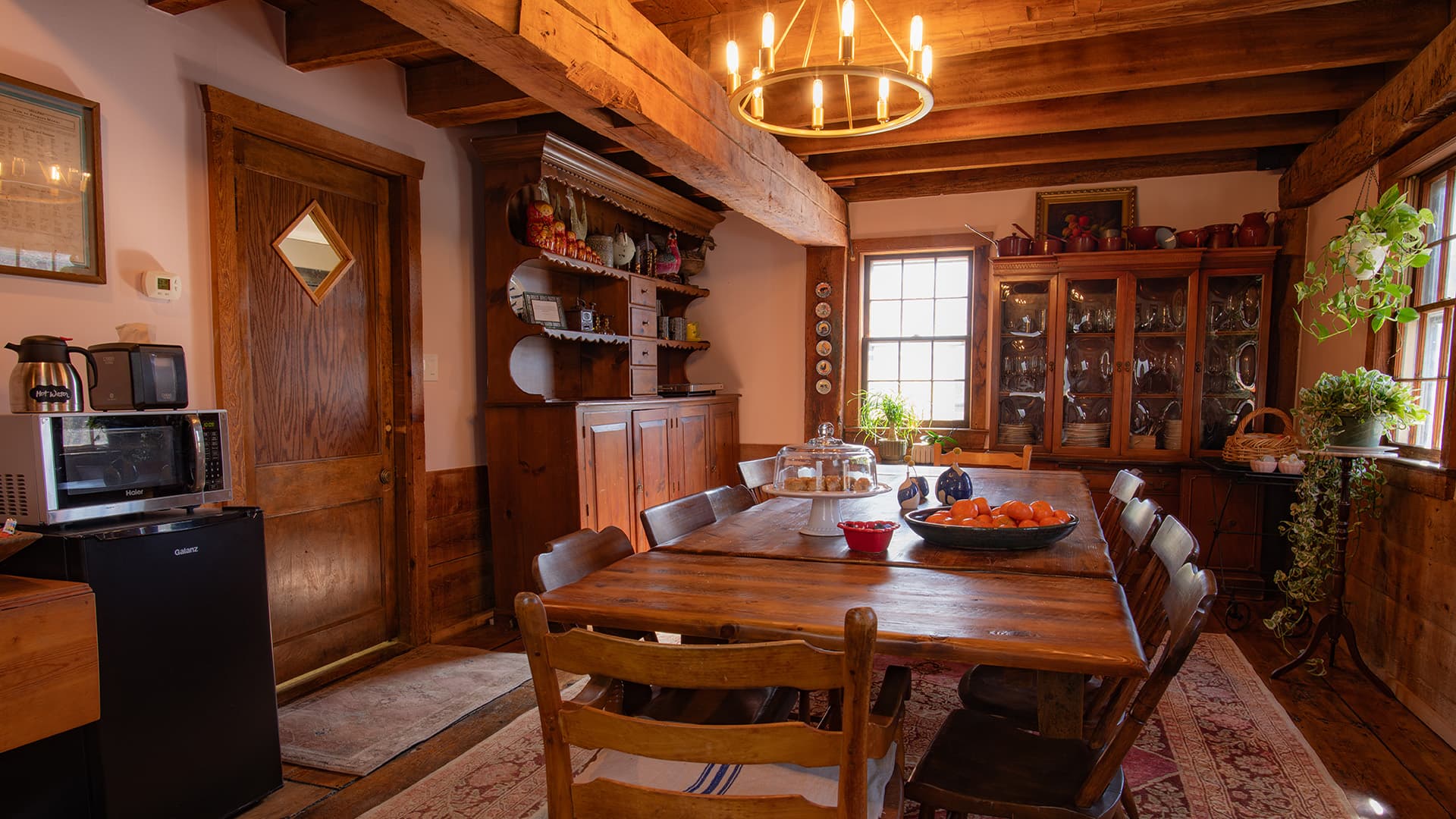 A cozy, rustic dining room featuring a long wooden table, warm lighting, and various shelves with decor and dishes.